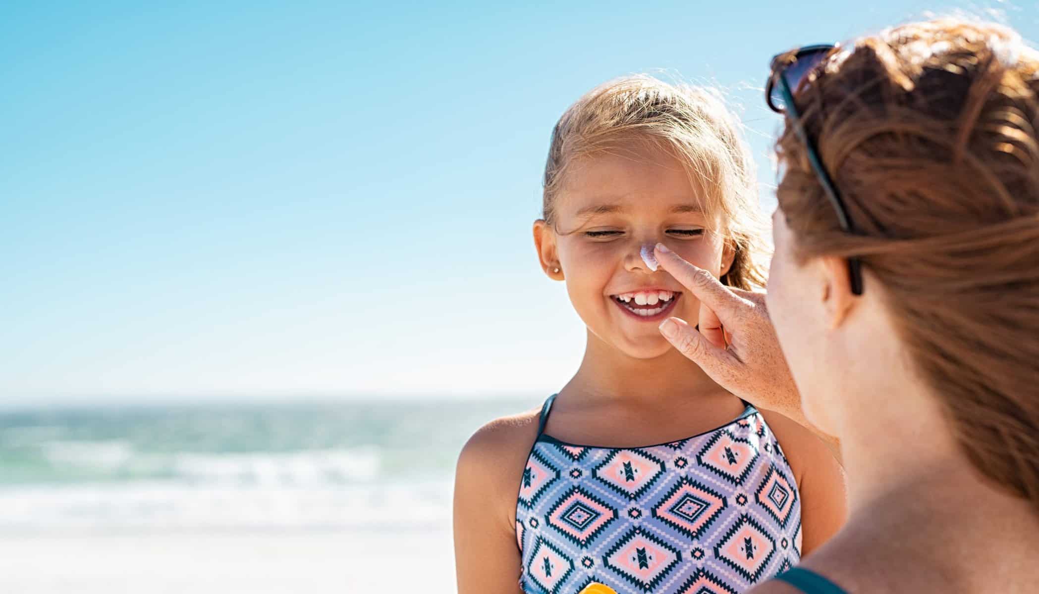 Young,Mother,Applying,Protective,Sunscreen,On,Daughter,Nose,At,Beach.